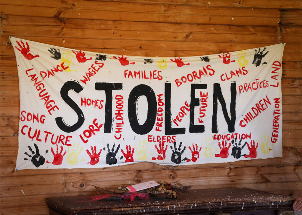 White canvas banner with the word Stolen painted in black surrounded by red and black hand imprints